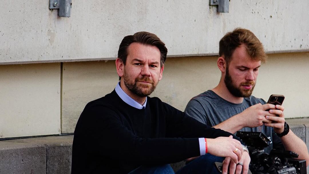 Thomas Kessler (Sportdirektor 1. FC Köln) sitzt vor Betonwand auf Stadion-Sitz und schaut in die Kamera.